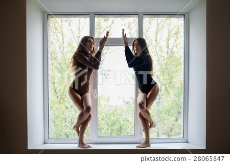 Two beautiful women doing yoga asana eagle pose on window sill 28065847
