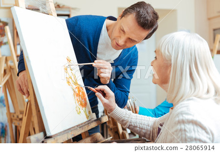 Serious artist helping elderly woman in painting Serious artist helping elderly woman in painting 28065914