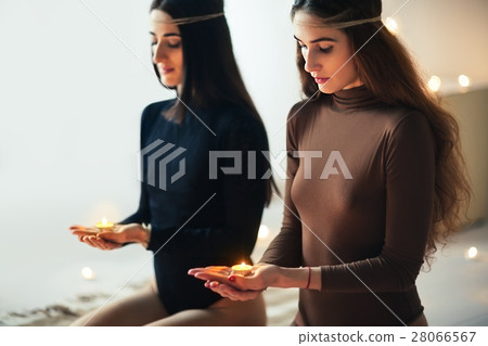 Two young women doing yoga asana diamond pose with candles in ha Two young women doing yoga asana diamond pose with candles in ha 28066567