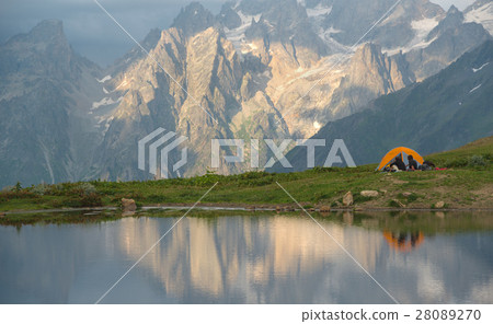 Orange tent and tourists near mountain lake Orange tent and tourists near mountain lake 28089270