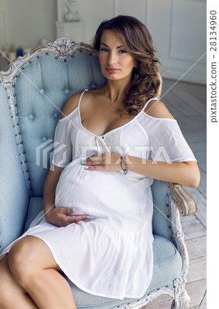young pregnant woman in white dress sitting in 28134960