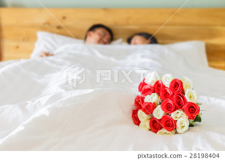 Bouquet on the white bed and blur of couple in hotel room Bouquet on the white bed and blur of couple in hotel room 28198404