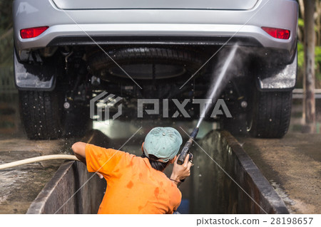 Man spraying pressure washer for car wash in car care shop. Focus on car 28198657