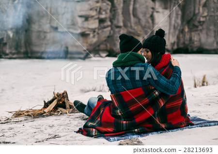 Couple sitting near a bonefire. They are covered Couple sitting near a bonefire. They are covered 28213693