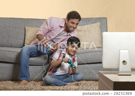 Father and son sitting on sofa playing video games Father and son sitting on sofa playing video games 28231369