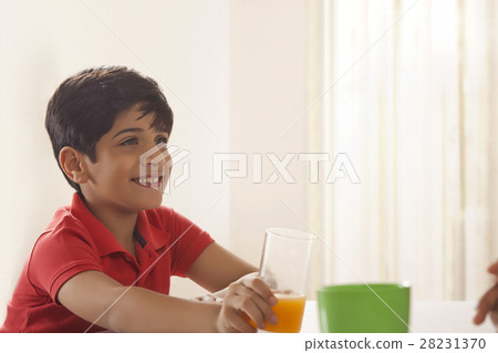 Boy holding glass of orange juice at dining table Boy holding glass of orange juice at dining table 28231370