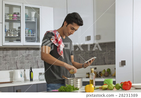 Young man cooking in kitchen using digital tablet 28231389