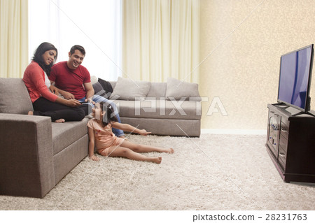 Mother, father and daughter sitting on sofa and watching TV 28231763