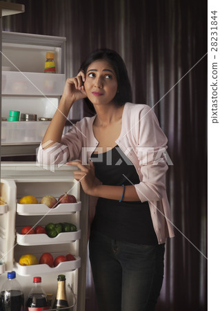 Young woman standing in front of open refrigerator looking tensed Young woman standing in front of open refrigerator looking tensed 28231844