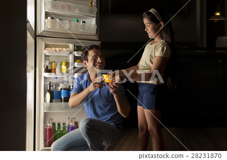 Father giving bowl to daughter from fridge at night 28231870
