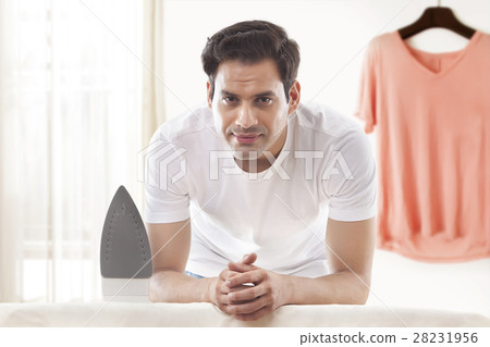Portrait young man with ironing board and top hanging on wall at home 28231956