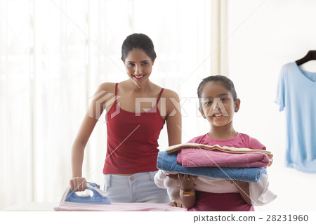 Mother ironing and her daughter holding folded laundry Mother ironing and her daughter holding folded laundry 28231960