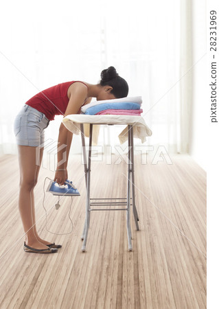 Young woman leaning on ironing board and holding iron 28231969