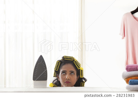 Young woman with curlers hiding behind ironing board 28231983