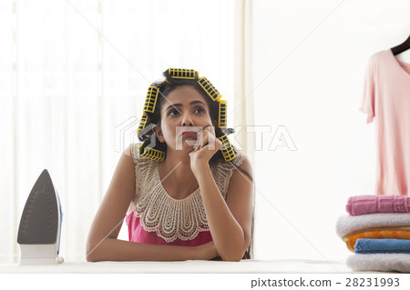Young woman with curlers sitting at ironing board 28231993