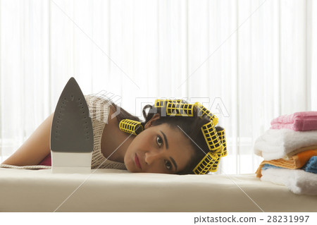 Young woman with curlers sleeping at ironing board 28231997