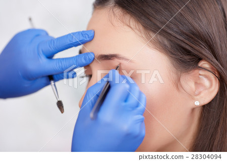 Professional in gloves plucking eyebrows for 28304094