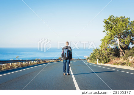 Young man with a backpack walks alone on a road 28305377