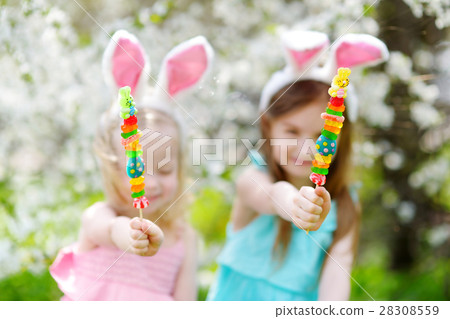 Two adorable little sisters eating colorful gum candies on Easter Two adorable little sisters eating colorful gum candies on Easter 28308559