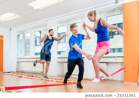 Physio practicing slacklining with athletes in gym Physio practicing slacklining with athletes in gym 28311301