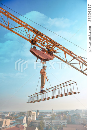 Crane holding construction with man over city. 28334117