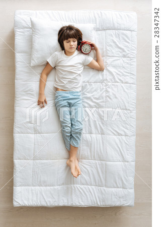 Relaxed boy lying in the bed with an alarm Relaxed boy lying in the bed with an alarm 28347342