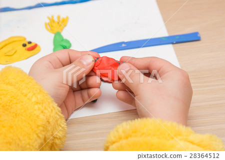 The child is holding a piece of red clay, close-up 28364512