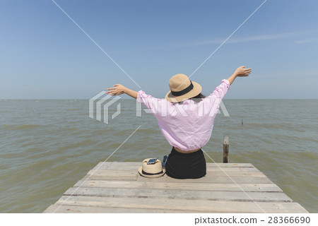 Woman raising her hands and siiting on wooden pier 28366690
