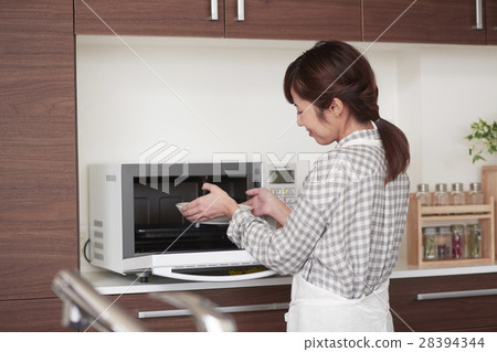 Women who stand in the kitchen and use a microwave Women who stand in the kitchen and use a microwave 28394344