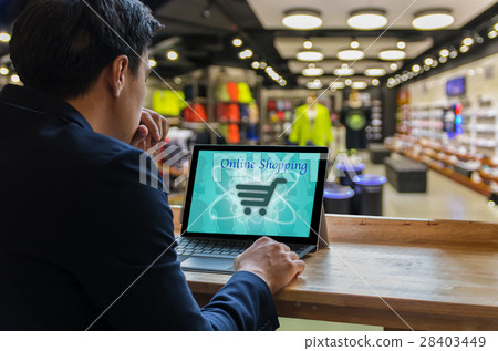 Businessman sitting and using computer laptop showing the shopping online beside the windows glass over the Abstract blurred photo of clothing store in a shopping mall, Business technology concept Businessman sitting and using computer laptop showing the shopping online beside the windows glass over the Abstract blurred photo of clothing store in a shopping mall, Business technology concept 28403449