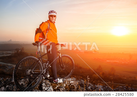 Sun rises behind man getting ready to ride his Sun rises behind man getting ready to ride his 28425580