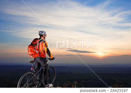 Sun rises behind man getting ready to ride his Sun rises behind man getting ready to ride his 28425587