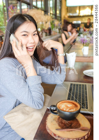 Woman at cafe use laptop and talking on phone Woman at cafe use laptop and talking on phone 28444366