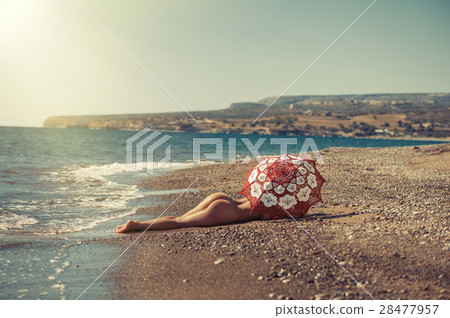 Beautiful naked girl lying on the beach under an u Beautiful naked girl lying on the beach under an u 28477957