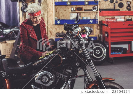 Smiling grandmother polishing bike in mechanic Smiling grandmother polishing bike in mechanic 28504134