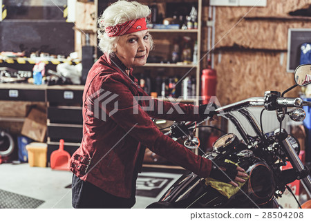 Smiling retiree polishing motorcycle in mechanic 28504208