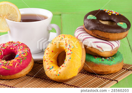 pile of glazed donuts with a cup of tea on a green 28560203