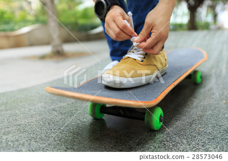young skateboarder tying shoelace at skatepark 28573046