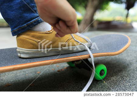 young skateboarder tying shoelace at skatepark 28573047