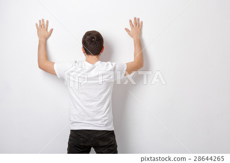 young man in white t-shirt with hands up near wall young man in white t-shirt with hands up near wall 28644265