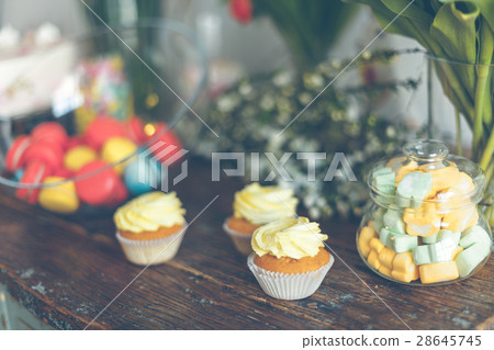Bright macaroons and cupcakes on a table Bright macaroons and cupcakes on a table 28645745