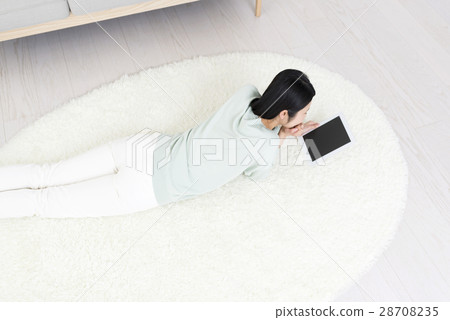 一名控制躺在她的耳朵上的平板電腦的年輕女子躺在她的臉上 一名控制躺在她的耳朵上的平板電腦的年輕女子躺在她的臉上 28708235