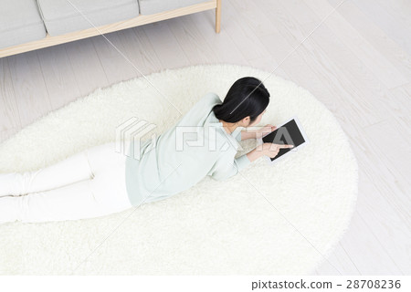 一名控制躺在她的耳朵上的平板電腦的年輕女子躺在她的臉上 一名控制躺在她的耳朵上的平板電腦的年輕女子躺在她的臉上 28708236