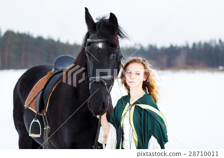 Young girl in dress with black horse in winter Young girl in dress with black horse in winter 28710011