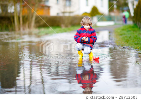 Little kid boy playing with paper ship by puddle Little kid boy playing with paper ship by puddle 28712503