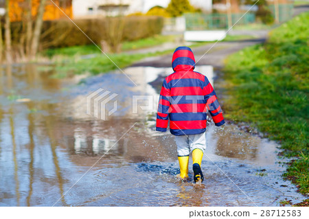 Little kid boy playing with paper ship by puddle Little kid boy playing with paper ship by puddle 28712583