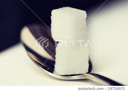 close up of white sugar cubes on teaspoon 28750072