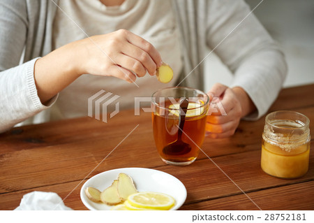 close up of woman adding ginger to tea with lemon close up of woman adding ginger to tea with lemon 28752181