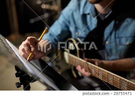 man with guitar writing to music book at studio 28755471