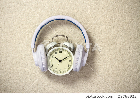 Retro alarm clock with white headphones on beige Retro alarm clock with white headphones on beige 28766922
